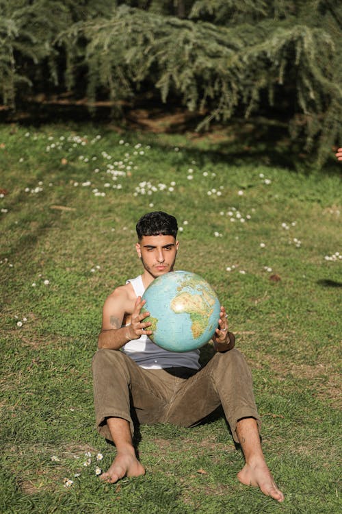 Man Sitting on Grass Holding a Globe