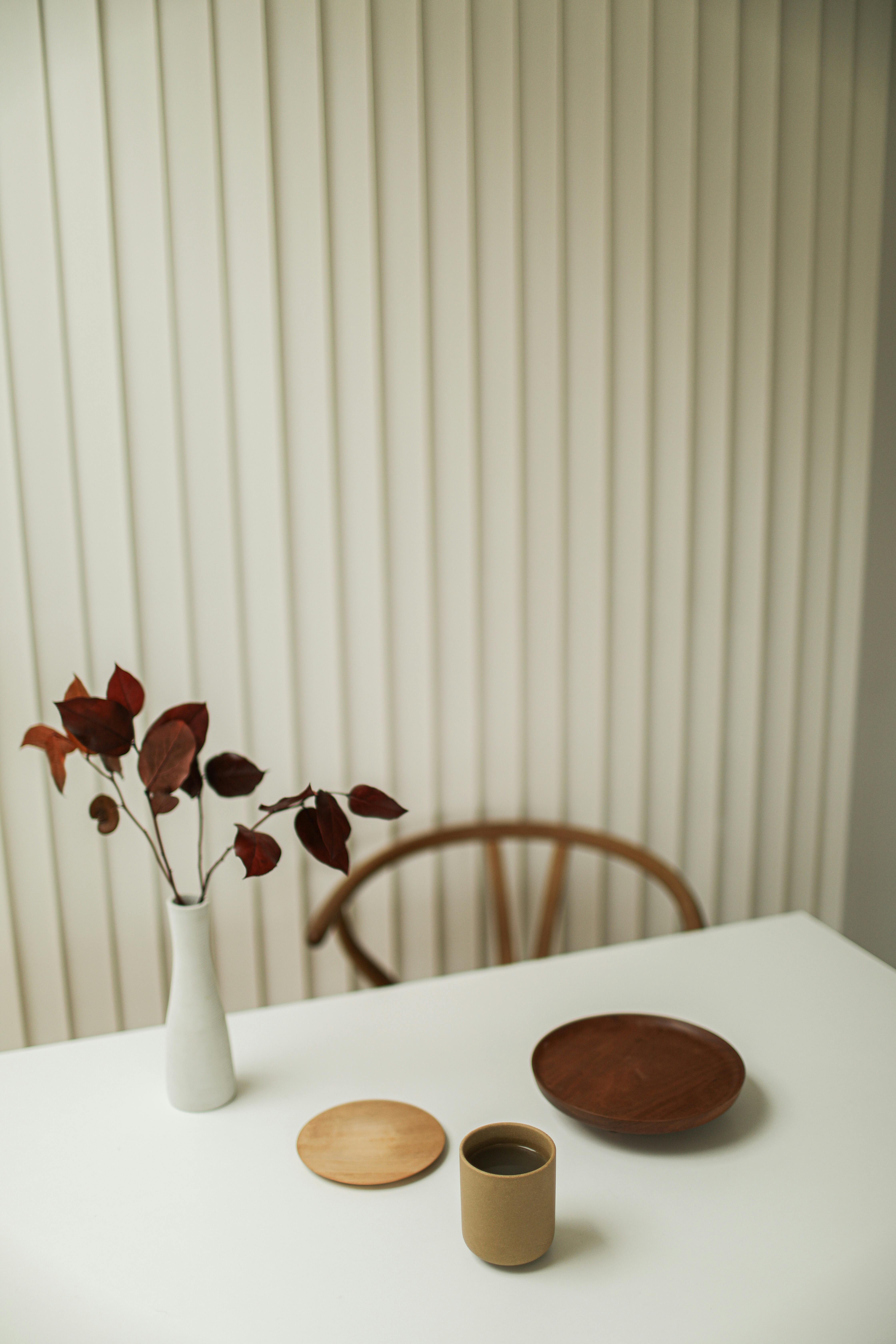 A minimalist setup featuring a ceramic vase, cup, and wooden elements on a white table.