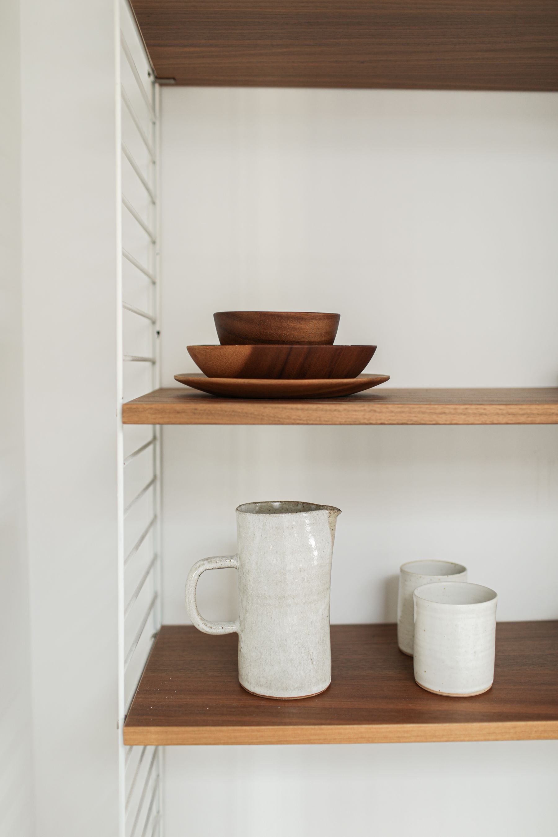 Minimalist open wooden shelves holding neatly arranged ceramic bowls and dinnerware