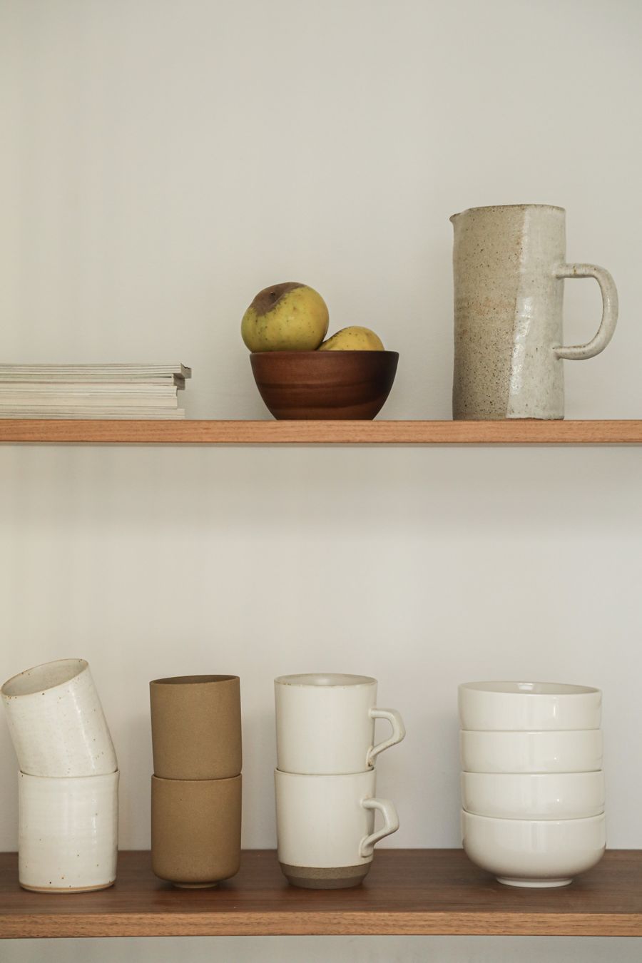 A sandstone-glazed pitcher and stacked cups on a warm kitchen shelf
