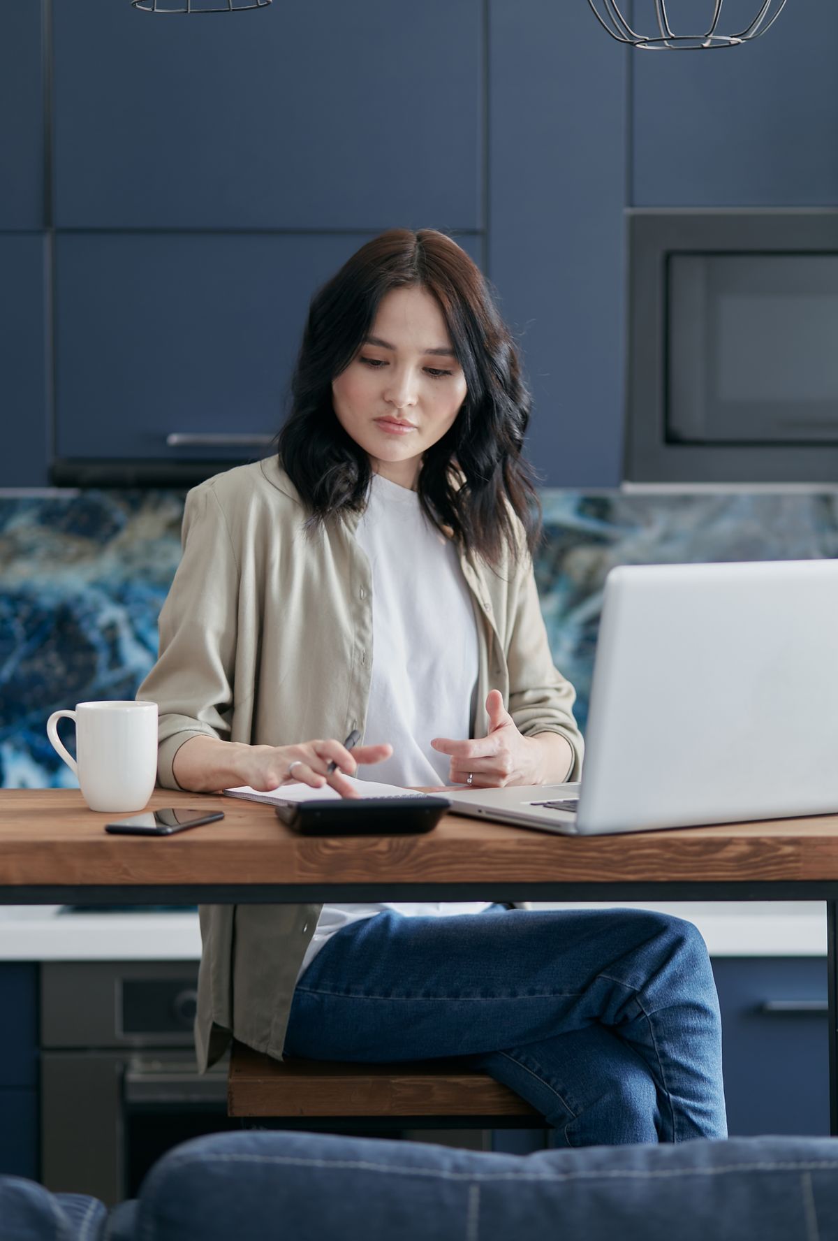Woman using laptop and calculator at home for finance management.