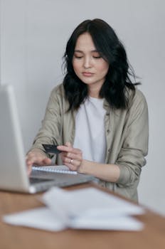 A young woman using a laptop and credit card for an online transaction in a business setting.