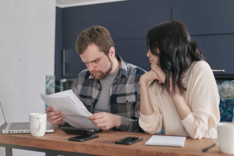 A Couple Sitting At The Table Looking At Documents