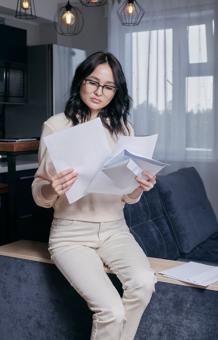 A Woman Wearing Eyeglasses Sitting On Couch Holding Documents