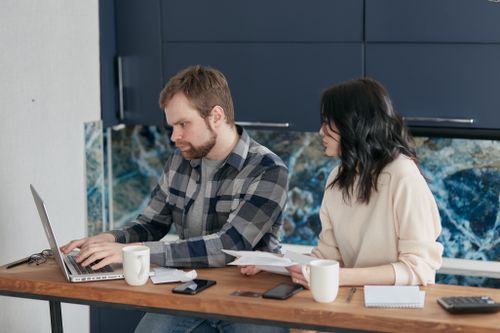 Free A couple working together at a home office desk with laptops and documents, collaborating on a project. Stock Photo