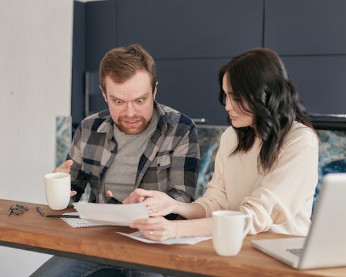 A Woman Showing a Document to a Shocked Man Sitting Beside Her
