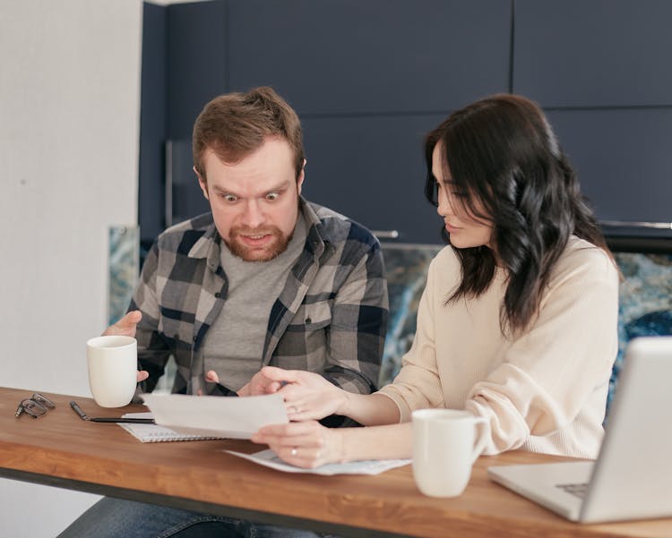 A Woman Showing A Document To A Shocked Man Sitting Beside Her
