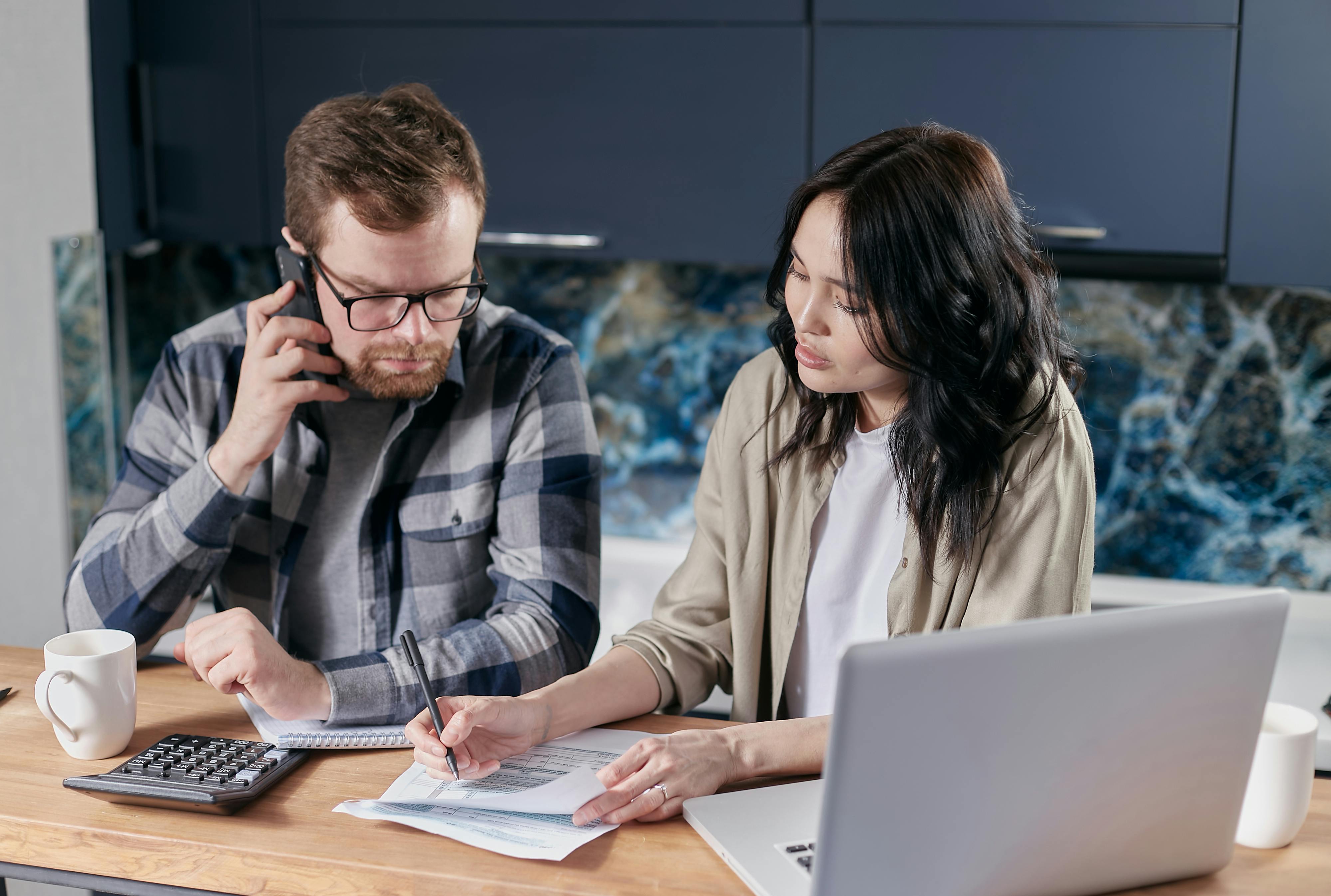 a man using a cellphone beside a woman filling out a form