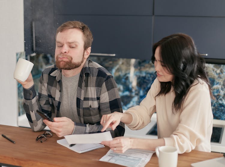 A Shocked Man Spitting A Drink Beside A Woman Showing A Paper