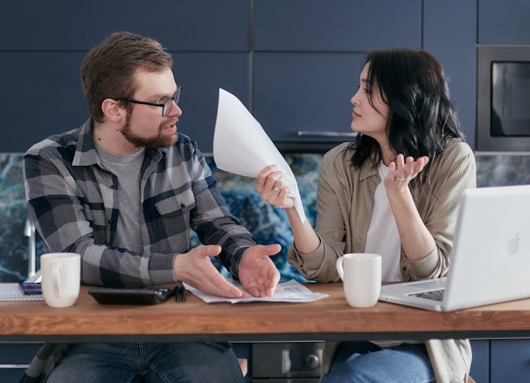 Man And Woman Sitting At Table With Laptop And Papers