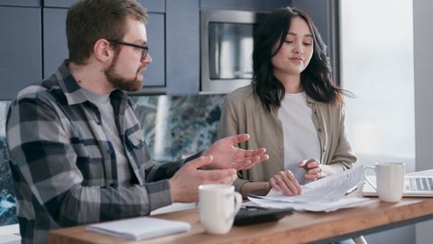 A couple reviewing financial documents in their kitchen, appearing focused and concerned.