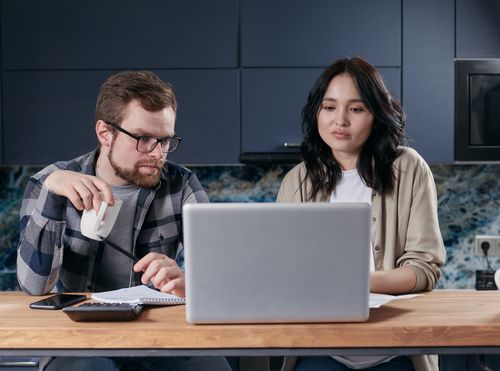 Free A couple working together on a laptop at a wooden table at home, focused on the screen. Stock Photo