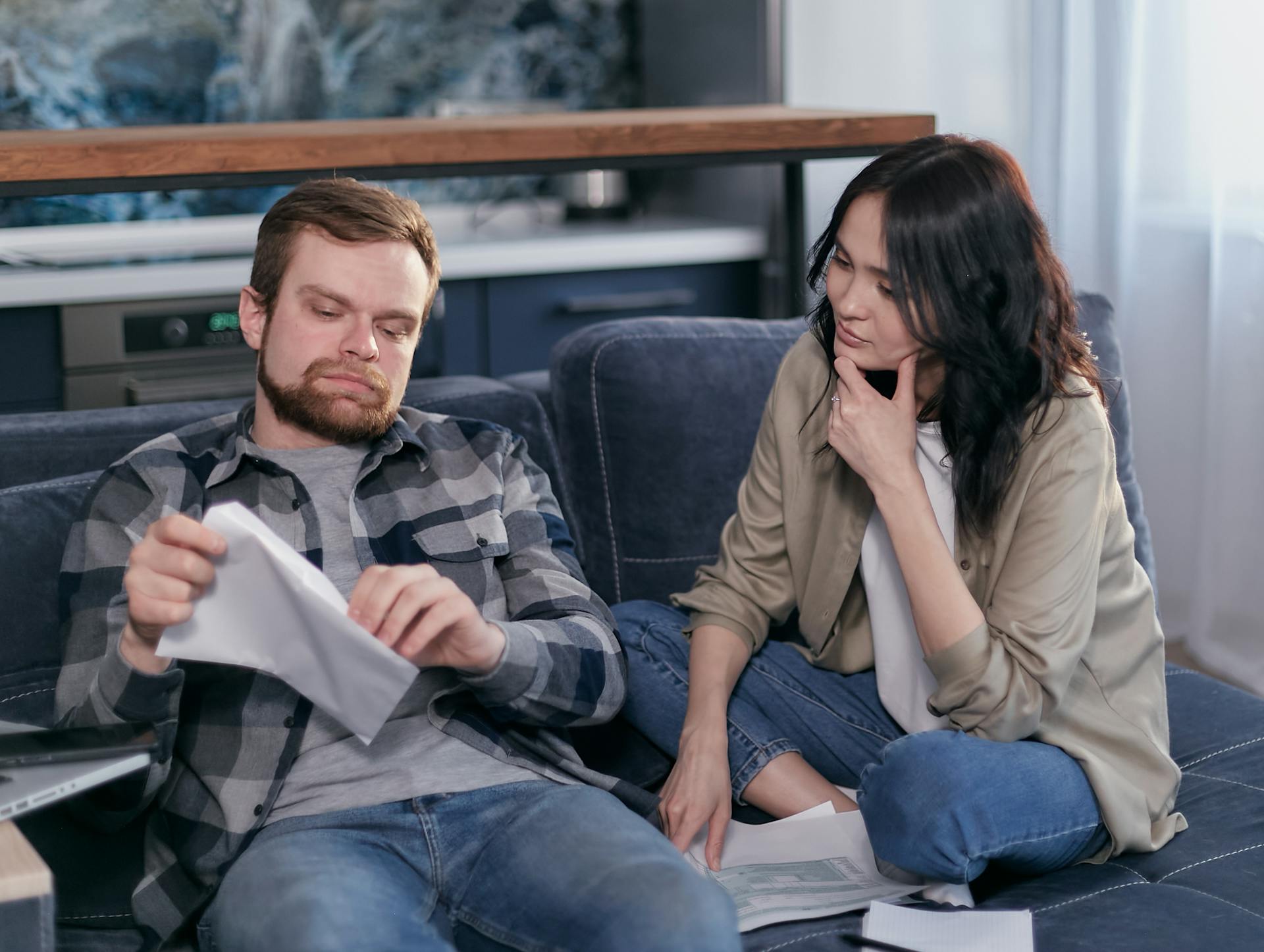 Couple at home reviewing bills and discussing finances on a couch.