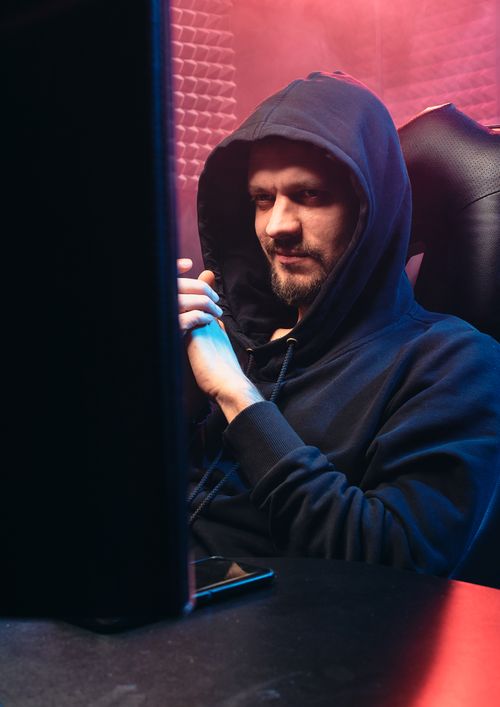 Free A stylish man sitting indoors wearing a black hoodie, smiling at his screen. Stock Photo