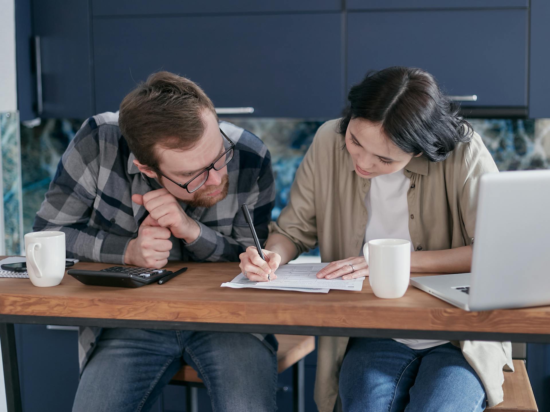 Couple reviewing financial documents together at a kitchen table with a laptop and calculator.