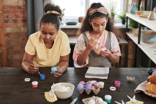 Free Two girls creatively painting Easter eggs at a table, enjoying a fun and colorful indoor activity. Stock Photo