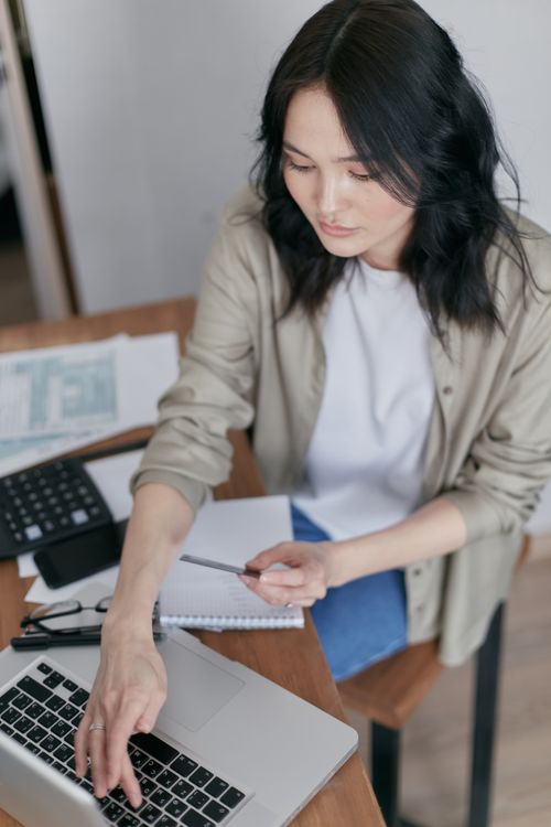 Free Focused woman working on a laptop at a wooden desk with office supplies. Stock Photo