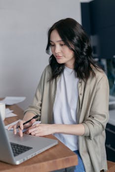 Young woman focused on work at desk with laptop, in a cozy office setting.