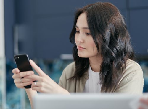 Free A young woman with black hair using a smartphone indoors, focused on the screen. Stock Photo