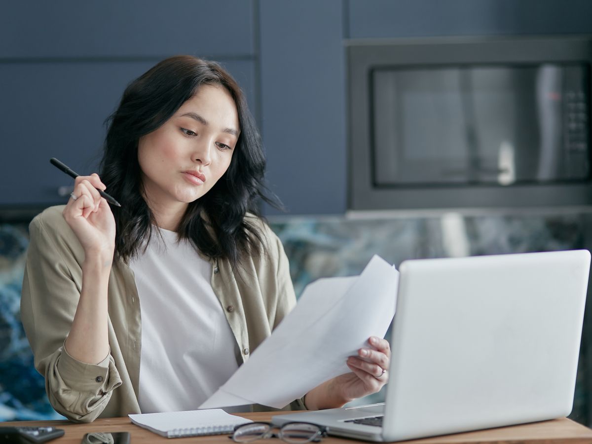 Vrouw bekijkt papieren en een laptop aan een tafel thuis