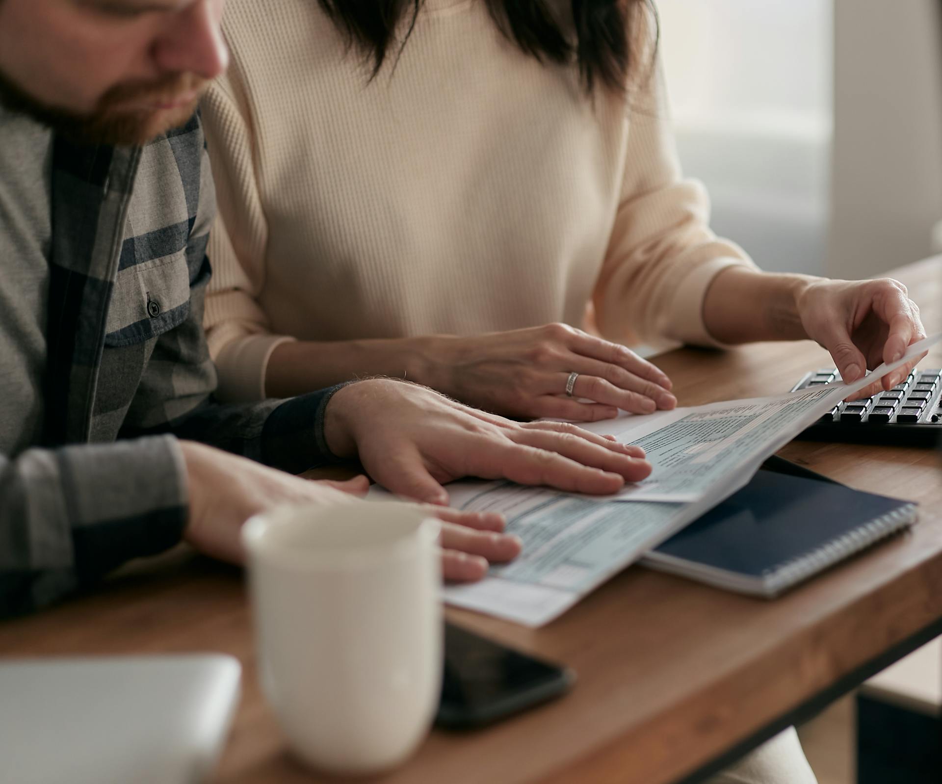 A man and woman reviewing financial papers at a wooden table with a keyboard and coffee mug.