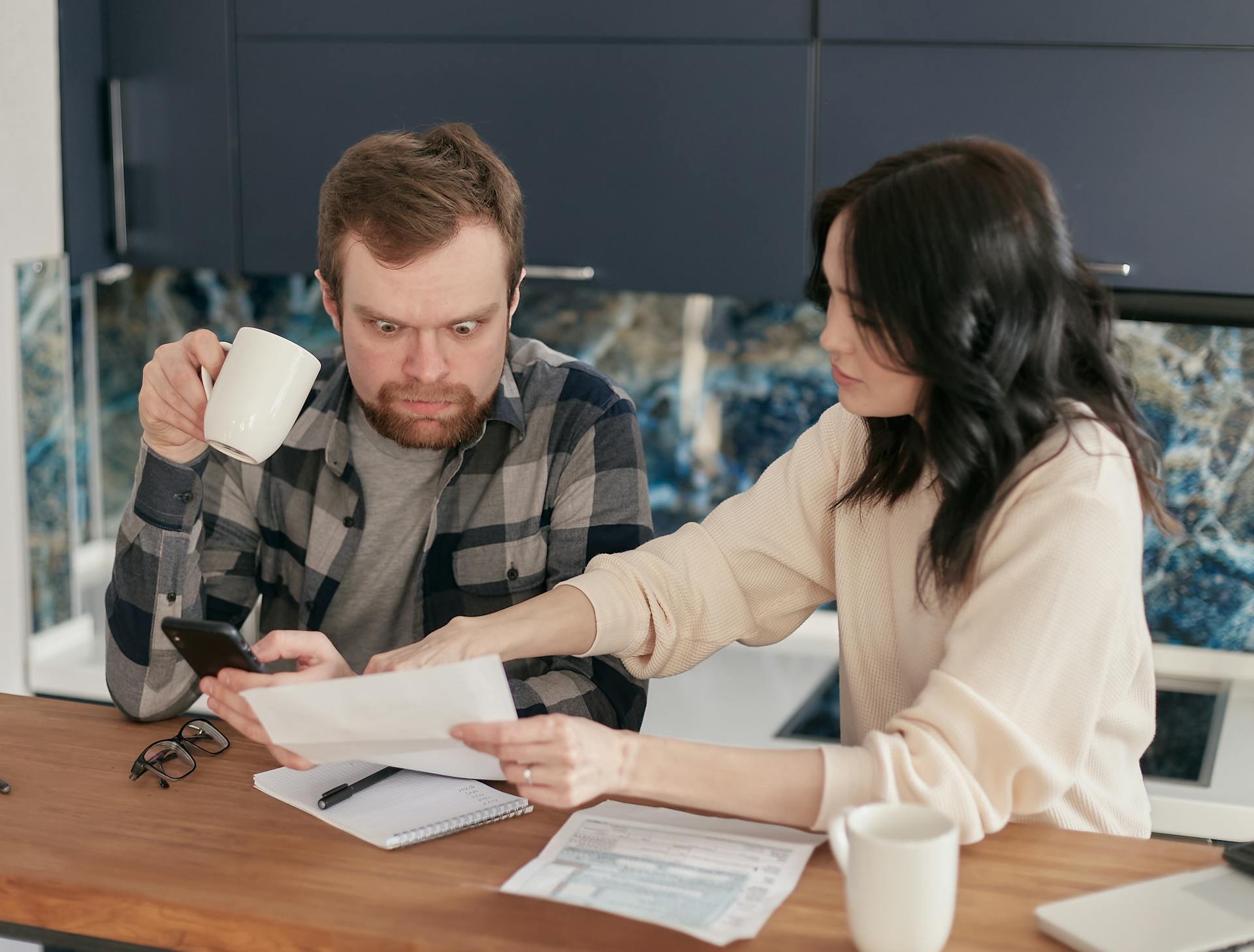 A couple looking concerned while reviewing financial documents at a wooden table.