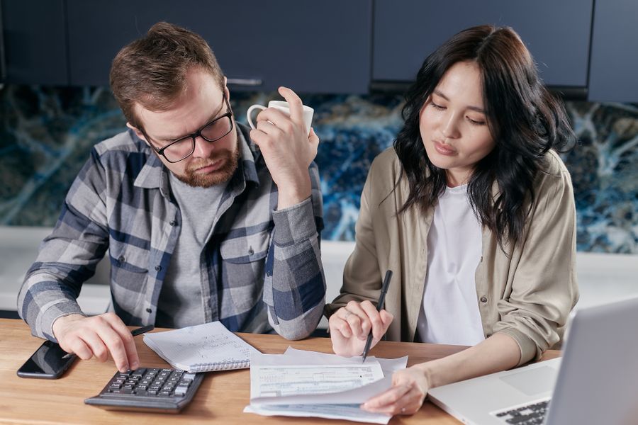 Two people going through household bills at a kitchen table with a laptop and calculator