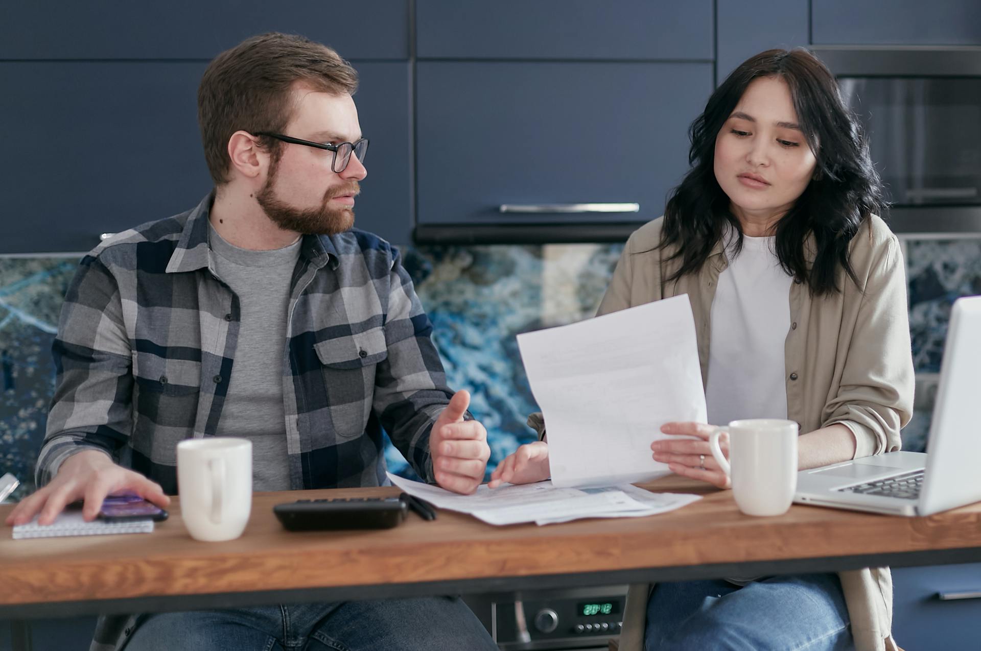 A couple sits at a table reviewing financial documents, looking concerned and focused.