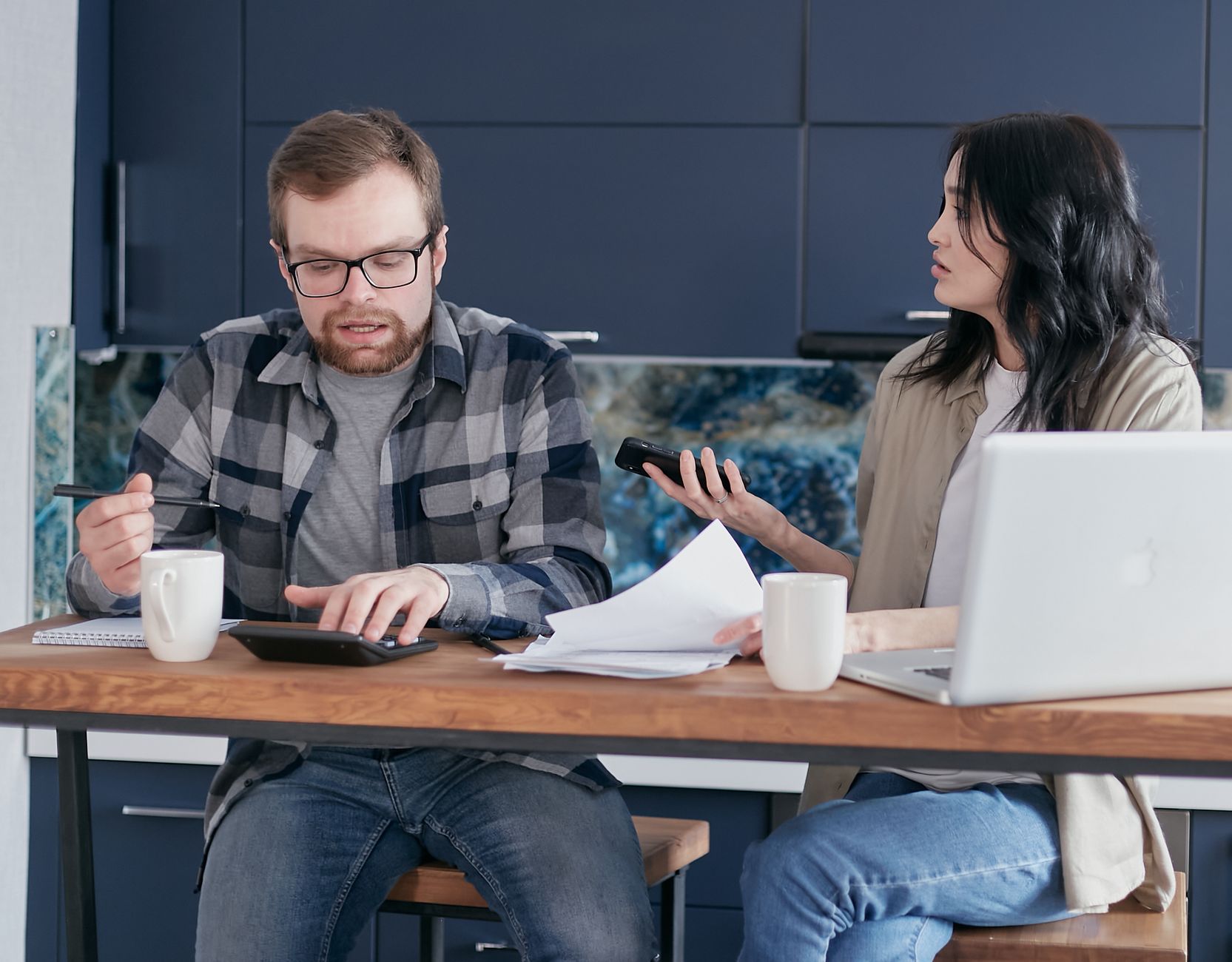 Two colleagues engaged in a work discussion around an office table, using a calculator and documents.