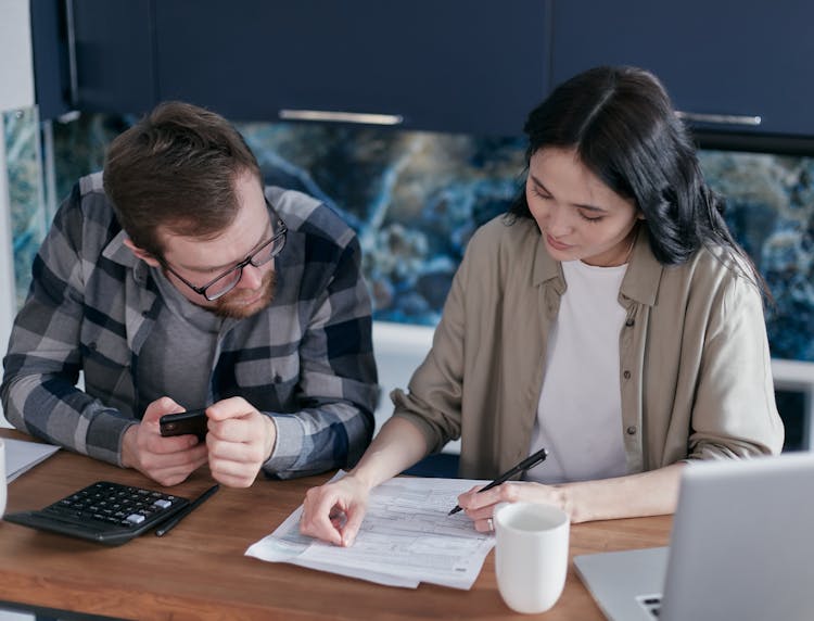 Man Holding A Cellphone Sitting Beside The Woman Signing Documents