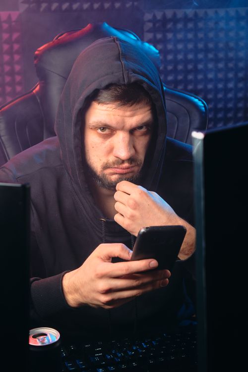 Free Mysterious man in hoodie using smartphone in a dark room, creating a moody atmosphere. Stock Photo
