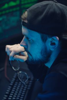 A bearded man in cap and eyeglasses intensely focusing on coding at a computer.