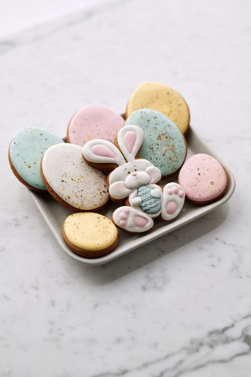 Free Colorful Easter cookies shaped like eggs and bunny on a white dish, perfect for spring celebrations. Stock Photo