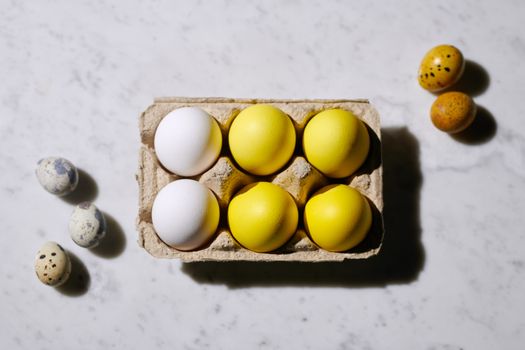Close-up of white and yellow Easter eggs with quail eggs on a marble surface.