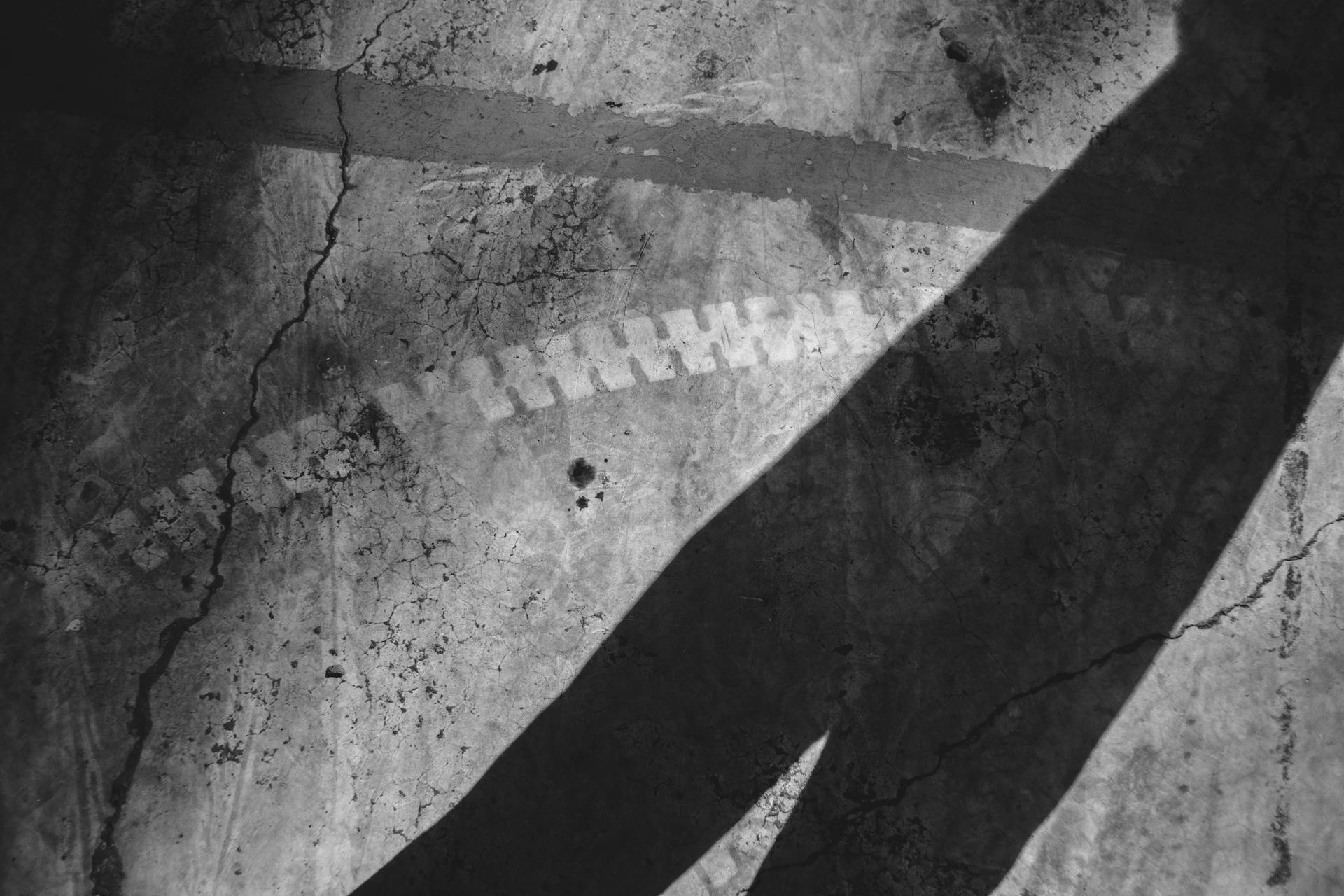 Black and white of linear shadow on cracked concrete wall with traces of dye