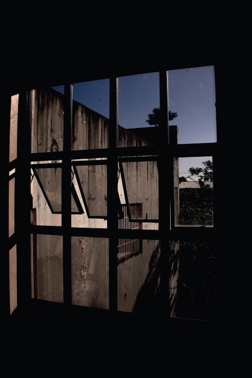 Abandoned gray building with shabby walls through window of dark room in evening