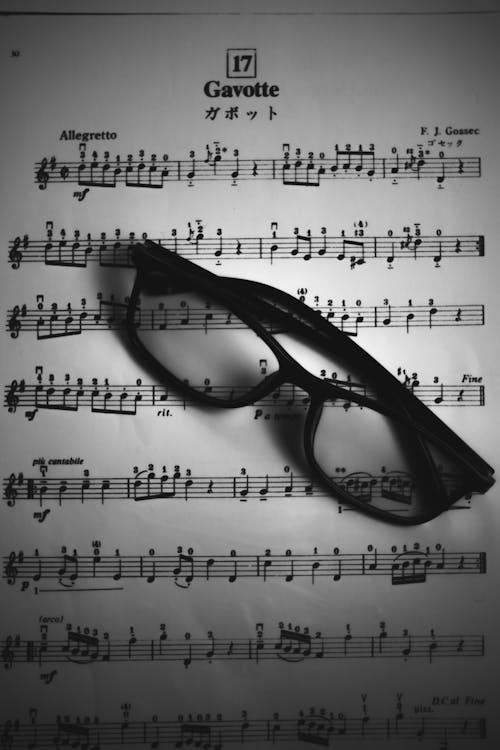 Black and white top view of black eyeglasses placed on page of opened music book with notes of musical composition