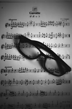 Black and white top view of black eyeglasses placed on page of opened music book with notes of musical composition