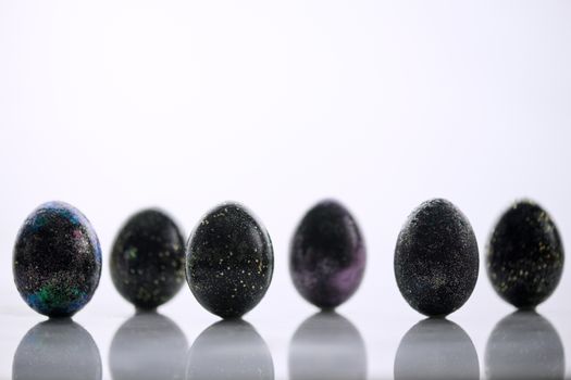 Black glittery painted eggs arranged on a smooth white surface.