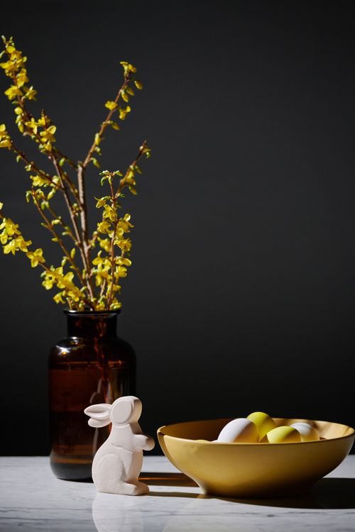 Free Elegant Easter scene with ceramic bunny and bowl of eggs, accented by yellow flowers in vase. Stock Photo