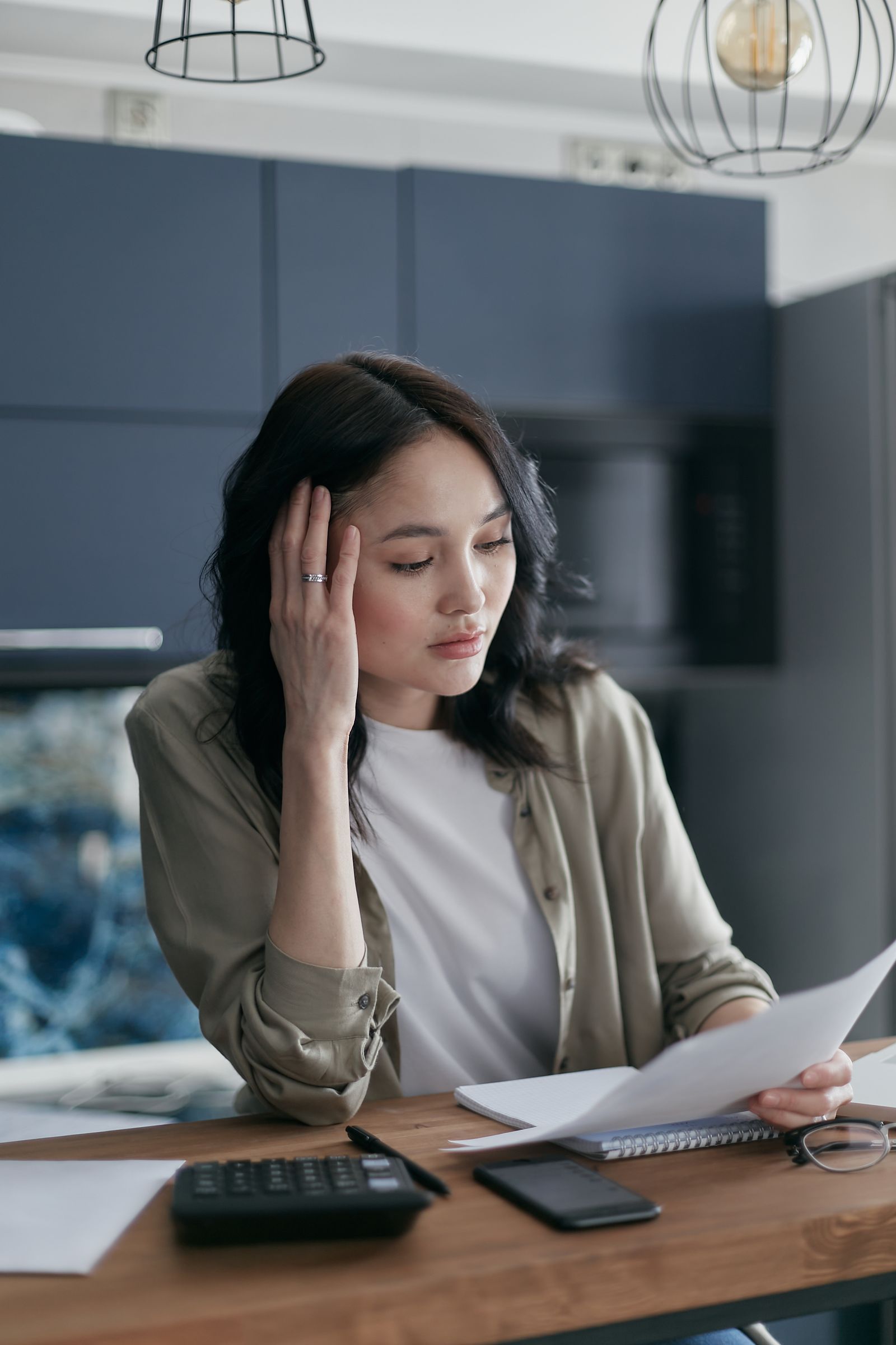Free A woman looks stressed while managing bills and documents at the kitchen table. Stock Photo