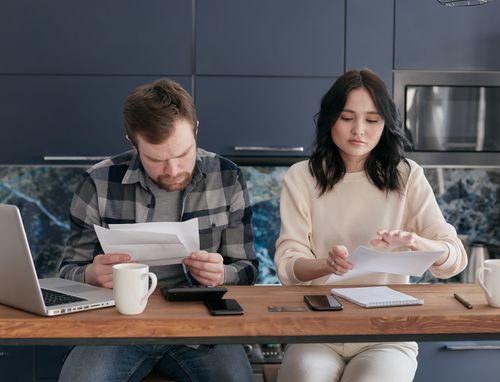 Free A couple reviews bills and manages finances on a kitchen table, looking concerned. Stock Photo