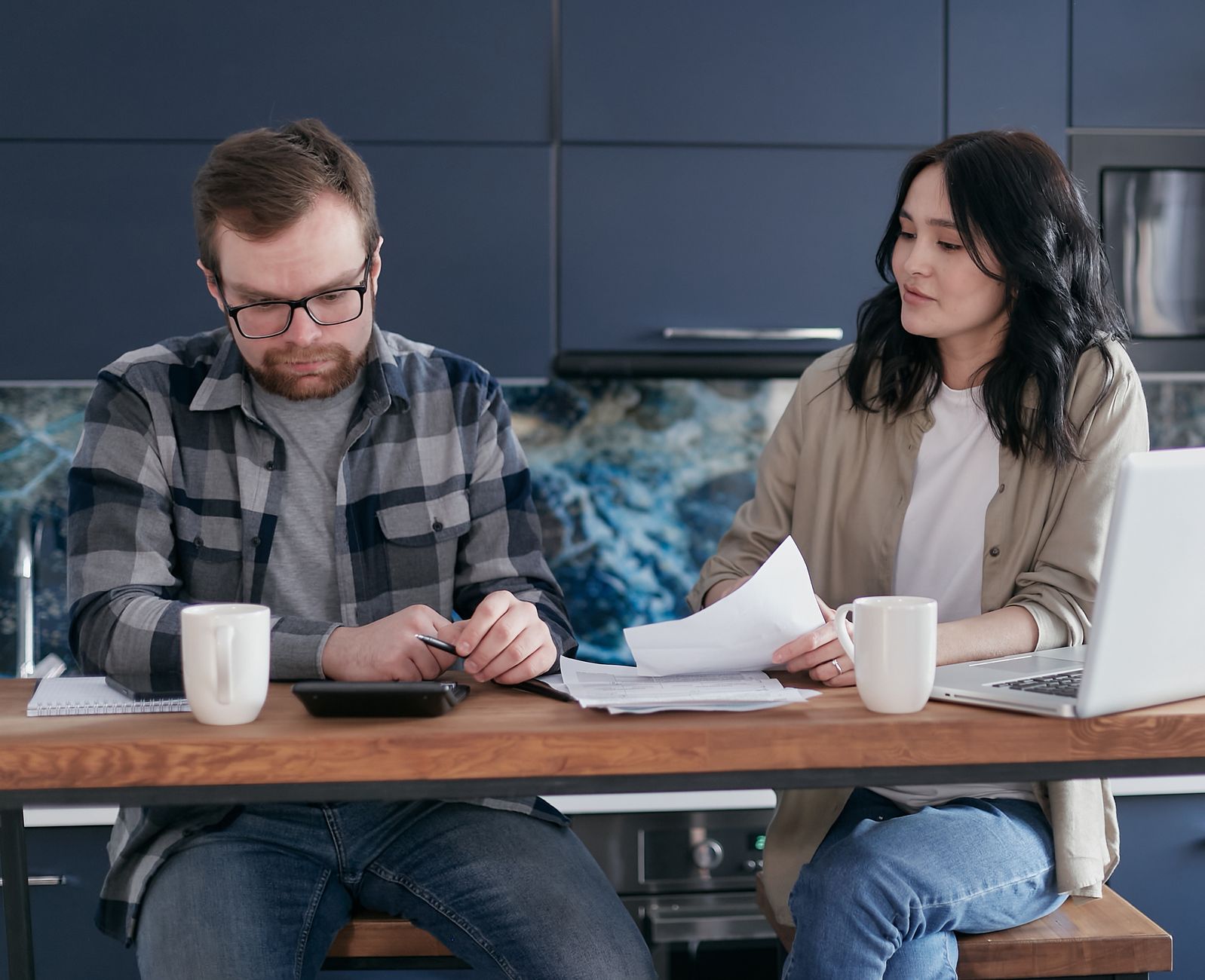 A couple working through bills with a calculator in a kitchen, the administrative version of a relationship argument.
