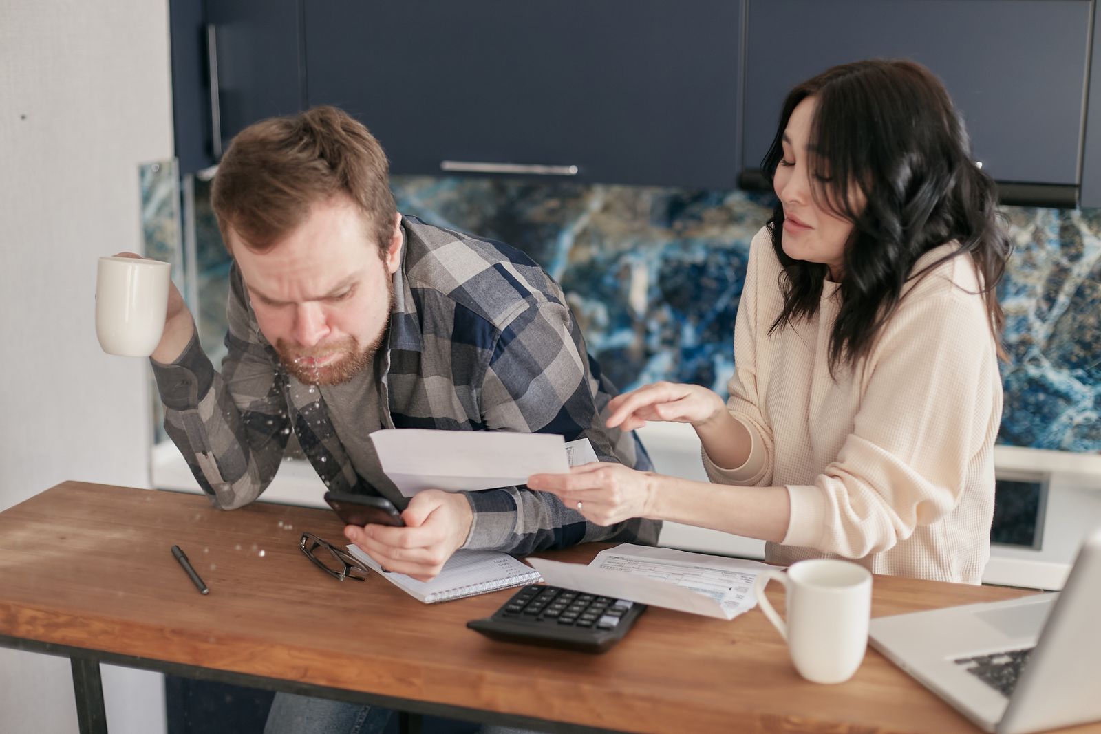 Asian couple reviewing bills, calculator and laptop while discussing household finances