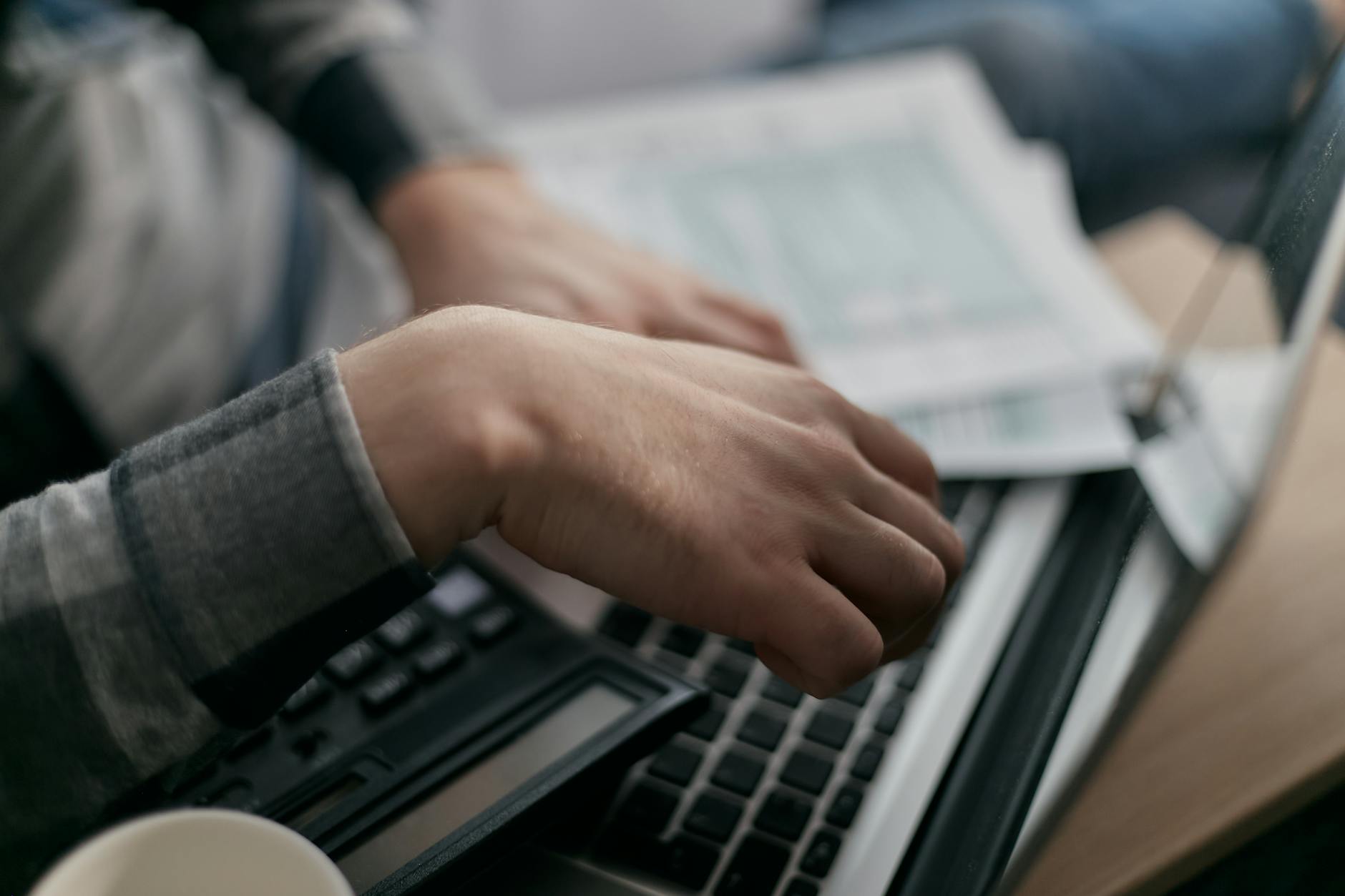 Close-up of hands calculating finances with a laptop and paperwork.