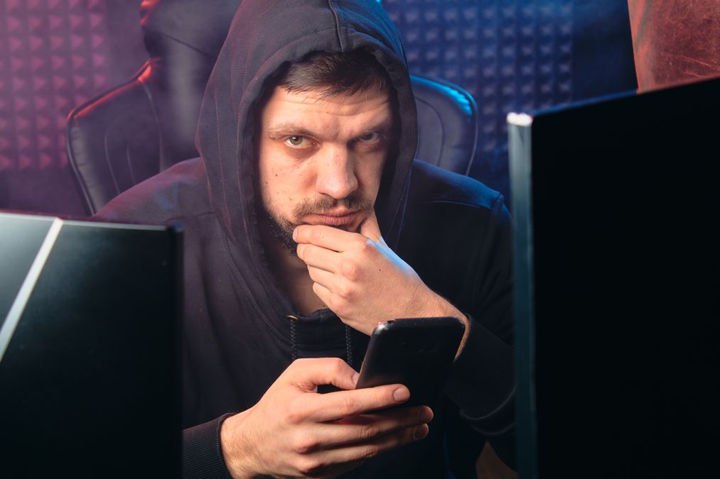 Homem de moletom escuro olhando preocupado para o celular diante de telas digitais, representando uma tentativa de golpe de phishing bancário