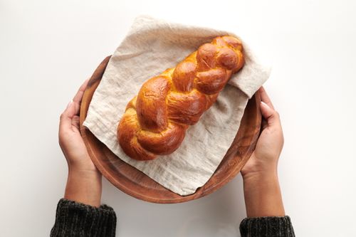 Top view of freshly baked challah bread held by hands on a wooden plate, perfect for traditional celebrations.