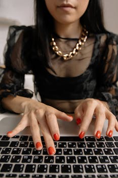 Fashionable woman wearing a chain necklace typing on a laptop, showcasing modern remote work style.
