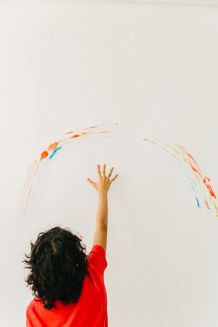 A Kid In Red Shirt Painting The Wall Using His Hand