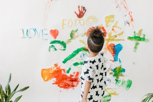A child engages in creative art on a white wall with vibrant colors indoors.